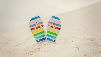 Flip flops shoes in color stripes on a white sand.