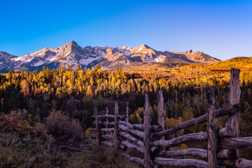 Dallas Devide in Colorado with western ranch style woden fence in the forgroud juxtaposed against golden aspens and whtie snow covered mountian vista