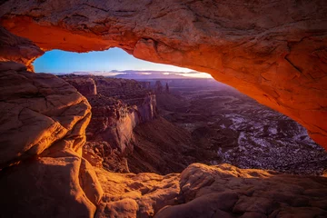 Fotobehang Mesa arch in Canyonlands National Park just outside Moab Utah. The sun creates an orange glow through the window of the desert arch.  The cold snow in the canyon contrasts the orange glow. © Thorin Wolfheart