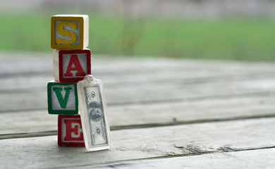 Child's multi color letter blocks forming the word "Save" with an old hundred dollar key chain leaning against the blocks on antique wooden floor board. Save, Invest, and retire concept.