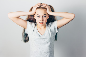 Emotional girl with stress or problems on gray studio background. Beautiful teen girl holding her...