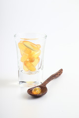 Cod liver oil omega 3 gel capsules on a wooden spoon object with glass medicine on white background