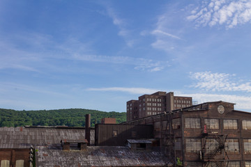 Fototapeta na wymiar Derelict industrial warehouse with modern commercial building and forested hillside beyond, horizontal aspect
