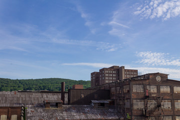 Fototapeta premium Derelict industrial warehouse with modern commercial building and forested hillside beyond, horizontal aspect