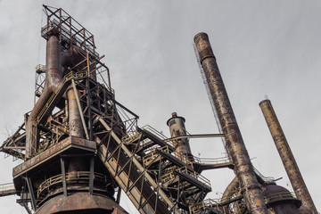 Fototapeta na wymiar Smokestacks and blast furnace, steel industry shapes against a gray sky, horizontal aspect