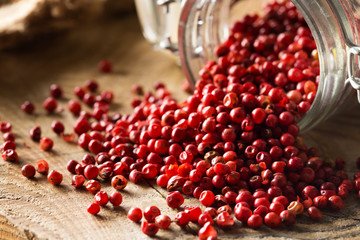 Pink or rose brazilian red peppercorns (schinus terebinthifolius) in glass jar on rustic wooden...