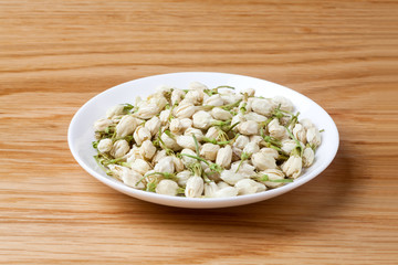 Dried jasmine flowers tea in a dish on wooden table.