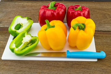 still – life concept colorful sweet bell pepper (capsicum)  and blue knife in white block   on wooden background