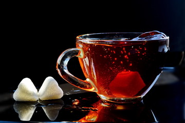 Glass Cup of brown black hot sweet tea with bubbles and splash from thrown dissolving piece of...