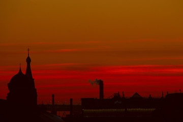 Naklejka premium Cityscape: silhouettes of churches, industrial pipes and city roofs at sunset