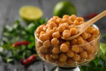 Wooden spoon in a glass bowl with boiled chickpeas with pepper and herbs.