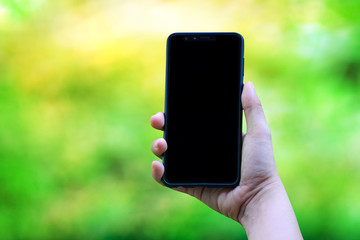 Close up woman hand holding modern black smartphone mock up in vertical position with blank screen against blurred grass background. Clipping path inside.