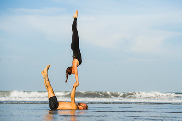 young attractive and beautiful acrobat couple practicing acroyoga exercise concentrated keeping balance practiing yoga on the beach in relaxation and meditation concept