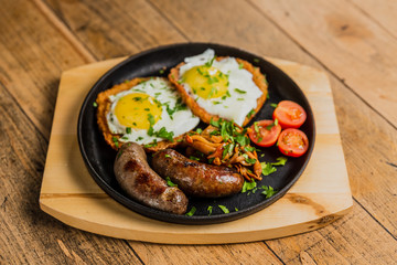 Traditional potato pancakes with fried eggs, mushrooms, sausages and tomatoes served on a hot frying pan.