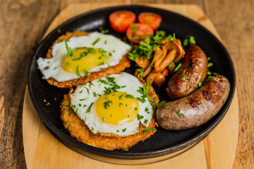 Traditional potato pancakes with fried eggs, mushrooms, sausages and tomatoes served on a hot frying pan.
