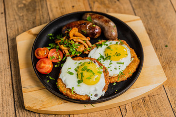 Fototapeta na wymiar Traditional potato pancakes with fried eggs, mushrooms, sausages and tomatoes served on a hot frying pan.