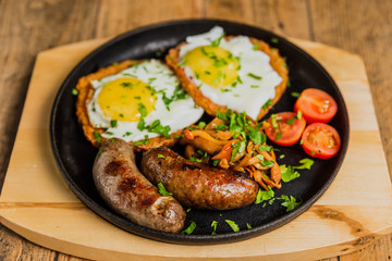 Traditional potato pancakes with fried eggs, mushrooms, sausages and tomatoes served on a hot frying pan.