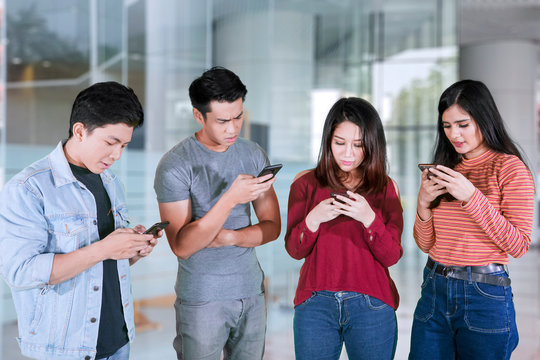 Four young people looks busy with mobile phones
