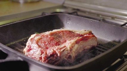 unrecognizable man chef hand puts a raw red beef steak on a black hot grill pan, close up view slow motion video in 4K