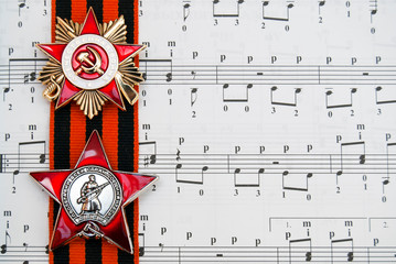 Soviet military orders (Order of the Patriotic War, Order of the Red Star) and St. George ribbon on the background of the notes for the song "Katyusha". May 9 is a Russian holiday, the day of victory.