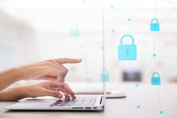 Select the security icon on the virtual display. Side view of female hand typing keyboard and aiming or pointing finger to the laptop screen.