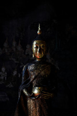 Ancient standing buddha image statue covered in gold leaves on dark background with Thai traditional mural painting art in Thai temple or Wat Suthat Bangkok Thailand. Buddhism belief and faith.