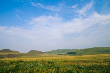 Blue sky with white clouds, green fields and hills