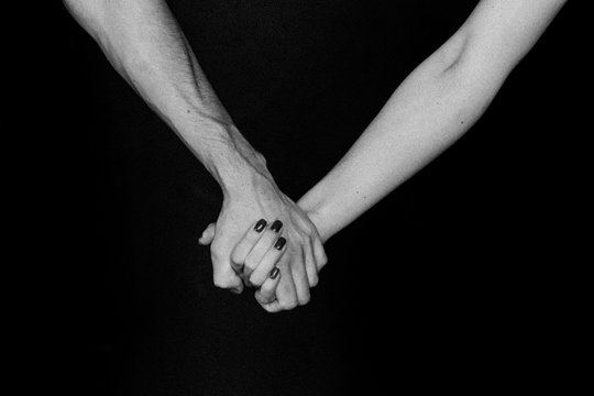 Two hands, male and female hand, holding hands, hands on a black background, black and white photo