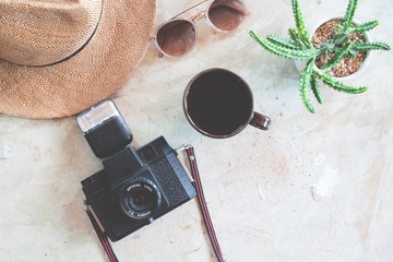 Creative flat lay of camera, coffee, trendy sunglasses, straw hat and pottery cactus on concrete background. Travel lifestyle concept.