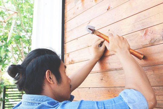 Asian Man Nailing Wooden Wall. Home Improvement Concept