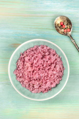 A bowl of pink Himalayan sea salt with a mix of peppercorns, shot from the top on a teal blue background with a place for text