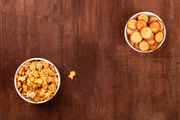 Salty crackers and goldfishes, shot from above on a dark wooden background with copy space. Party snacks banner with a place for text