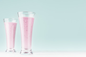 Healthy dairy dessert of ripe blueberry in two transparent high glass on white wood board and pastel green mint background, copy space.