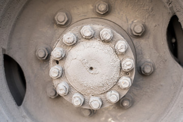The hub of the rear wheel of the bus or a large machine with bolts and nuts, covered with road mud sand and salt mixture  Dirty wheel of the bus wheel hub bearing in the daylight