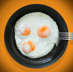 Breakfast of three eggs in a cast-iron pan on an orange background. View from above.