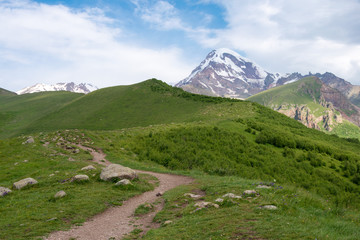 Fototapeta premium Kazbegi, Georgia - Jun 29 2018: Mountain range on a hiking trail from Gergeti Trinity Church to Gergeti Glacier. a famous landscape in Kazbegi, Mtskheta-Mtianeti, Georgia.