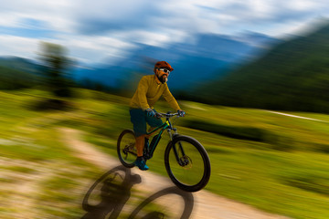 Single mountain bike rider on electric bike, e-mountainbike rides up mountain trail. Man riding on bike in Dolomites mountains landscape. Cycling e-mtb enduro trail track. Outdoor sport activity.