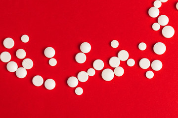 White pills spilling out of a toppled white bottle on red background