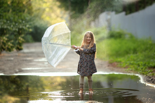 girl with long hair and with an umbrella in a beautiful dress and shoes runs through a puddle in the rain