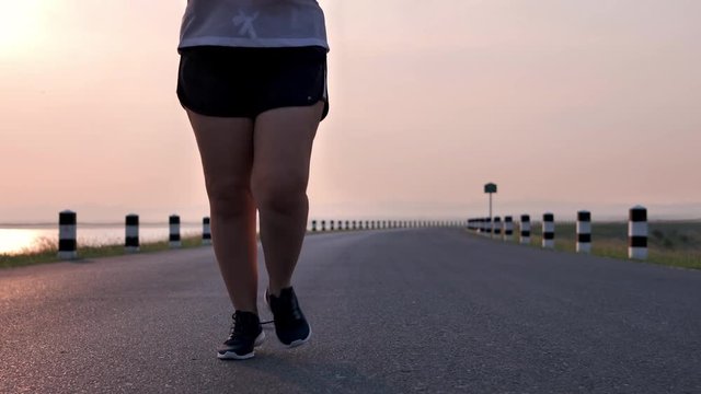 Overweight Asian women jogging in the street in the early morning sunlight. concept of losing weight with exercise for health. Slow motion, Bottom view