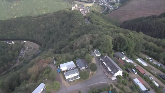 Panoramic approach towards the front of Bourscheid castle in Luxembourg. Showing the mountains, forest, village and river in the back. Sunny weather with clouds.