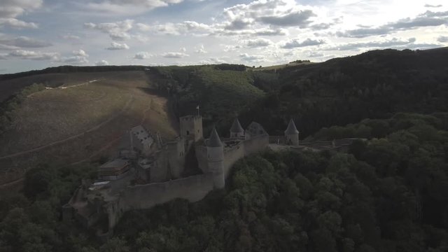 Panning left to right from the side of Bourscheid castle in Luxembourg. Showing the mountaints, forest and village in the back. Sunny weather with clouds.