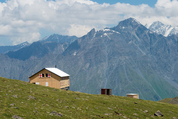 Fototapeta na wymiar Kazbegi, Georgia - Jun 29 2018: Mountain hut at Mountain range on a hiking trail from Gergeti Trinity Church to Gergeti Glacier in Kazbegi, Mtskheta-Mtianeti, Georgia.