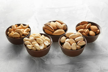 Bowls with different tasty nuts on grey background