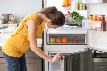 Pregnant woman taking food out of fridge at home