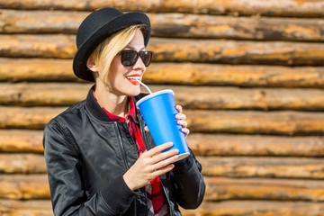 Smiling fashionable blonde drinking cola outdoors on wooden background