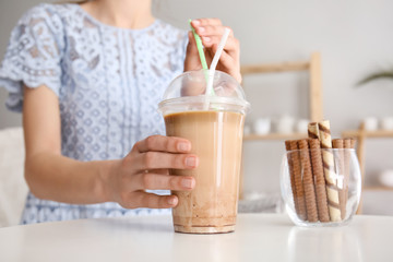 Woman drinking tasty frappe coffee at table