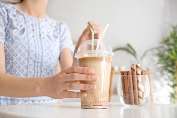 Woman drinking tasty frappe coffee at table