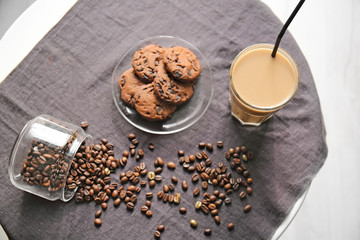 Glass of tasty frappe coffee with cookies and beans on table