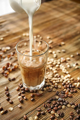 Pouring of milk from jug into glass on wooden table